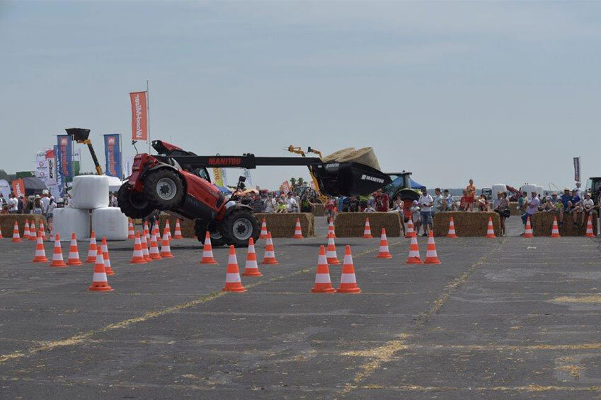 Opolagra Machine demonstration with tractor at outdoor trade fair, surrounded by spectators, hay bales, and banners.